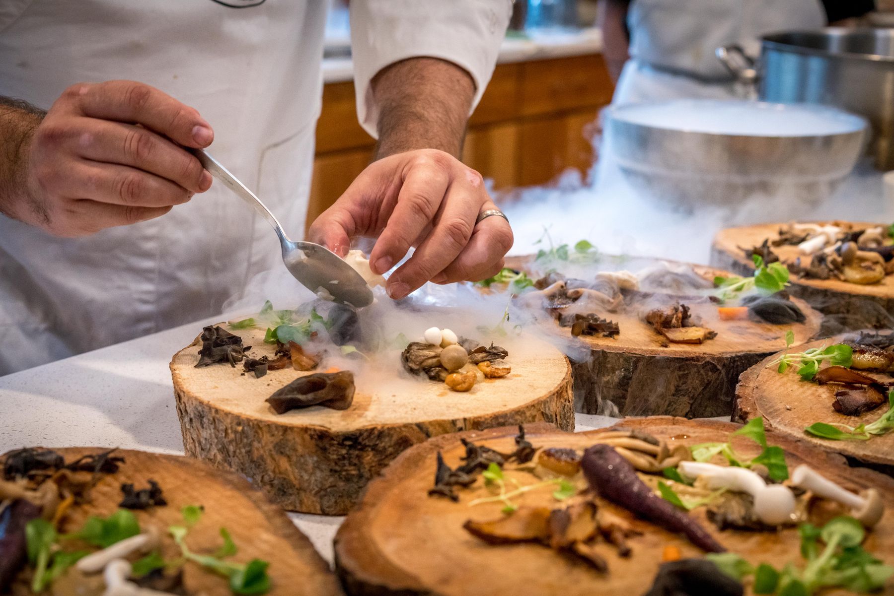 Chef plating a dish on a wooden pass