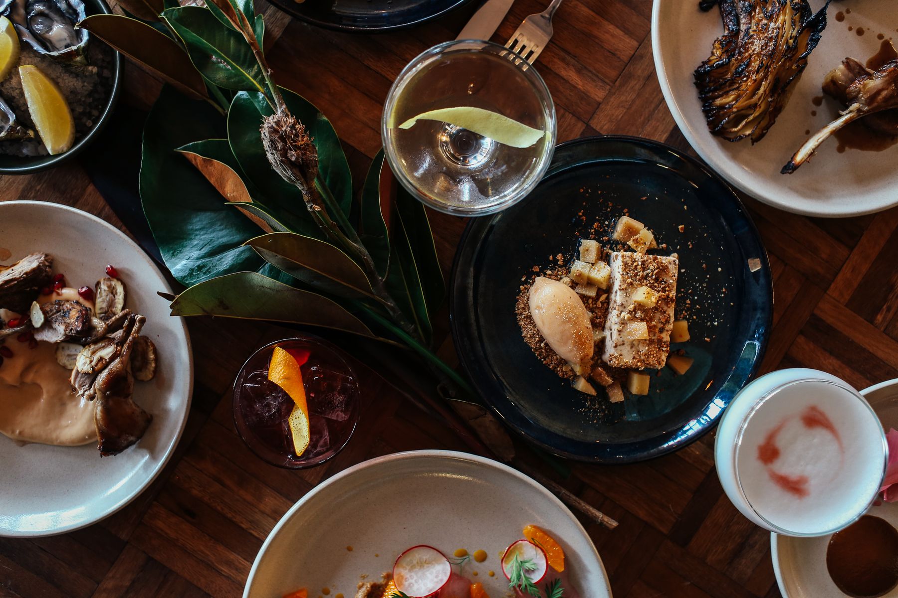 Overhead view of composed plates and a cocktail on a dark wood table