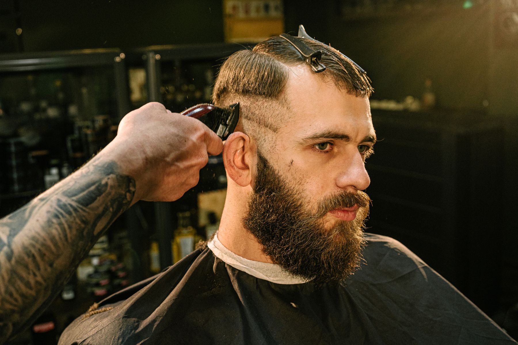 Barber running clippers above a bearded client's ear
